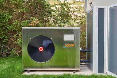 Eine Wärmepumpe in einem Garten neben einem Gebäude.